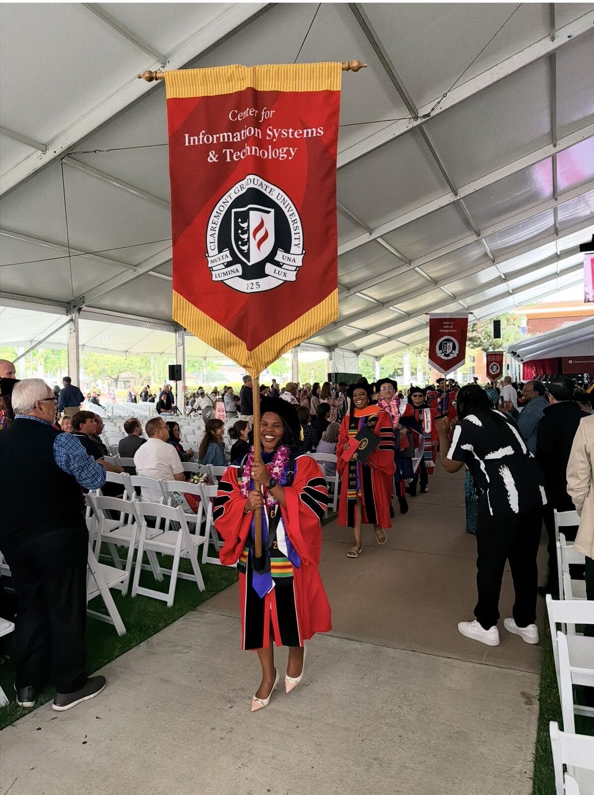 Maria at CGU Commencement, May 16, 2026 — Ph.D. conferred; carrying the CIST department banner.